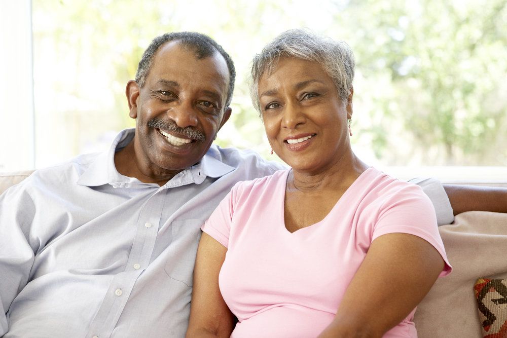 A happy middle-aged couple resting on a couch while smiling happily.