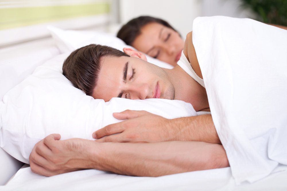 A closeup view of a handsome man sleeping while his wife sleeps peacefully in the background.