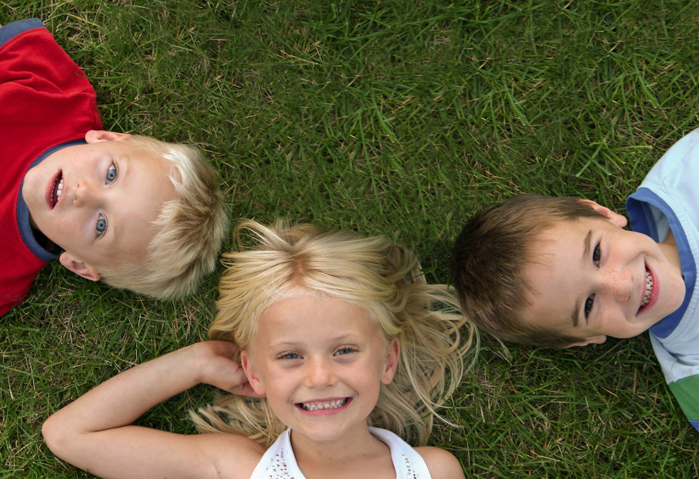 Two young boys and a young girl lying in the grass, smiling happily toward the sky.
